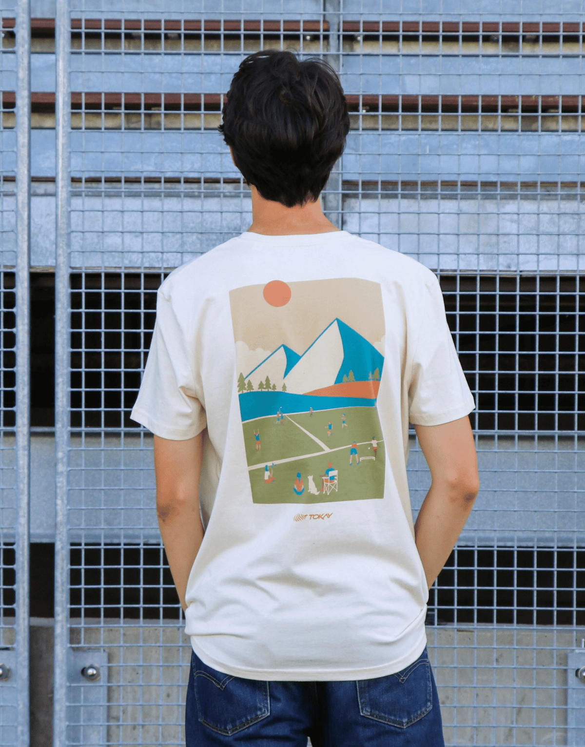 Person wearing a t-shirt with a graphic design of a field, mountains, and sun.